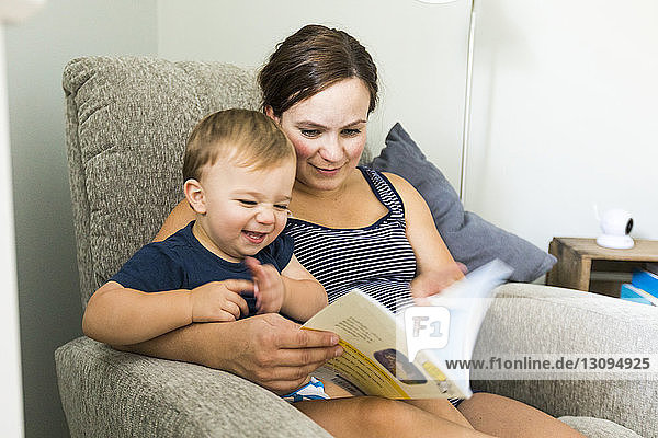 Mutter mit niedlichem Sohn liest Buch  während sie zu Hause auf einem Stuhl sitzt