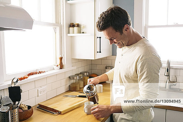 Happy man pouring coffee while standing by kitchen counter at home