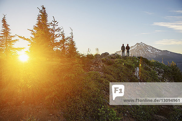 Rear view of hikers standing on mountain against sky during sunset