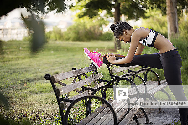 Sporty woman stretching leg on bench at park