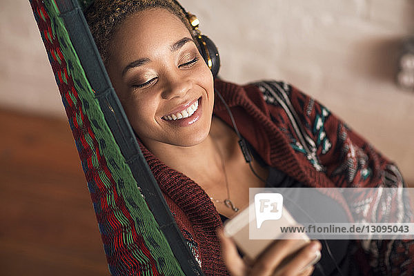 Glückliche Frau  die zu Hause auf der Hängematte über ein Smartphone Musik hört