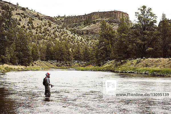Seitenansicht eines erwachsenen Mannes beim Fischen im Fluss am Berg