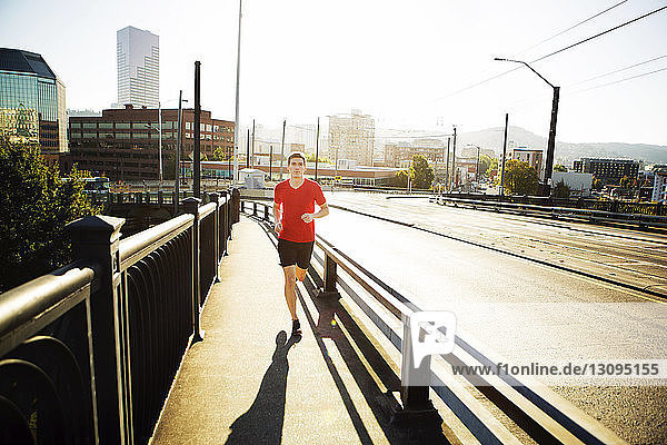 Full length of man jogging on footpath in city during sunny day