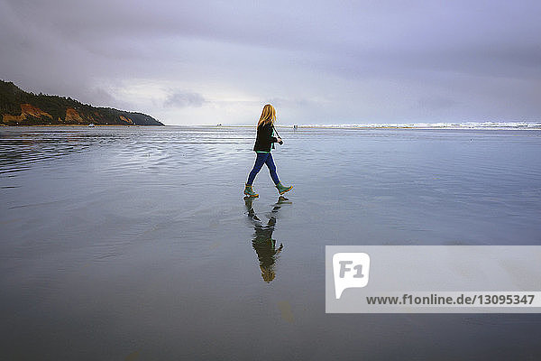 Seitenansicht einer Frau mit Kamera beim Spaziergang am Strand vor bewölktem Himmel