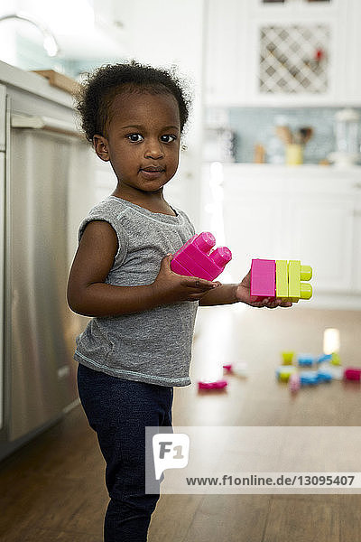 Porträt eines Mädchens  das Spielzeugblöcke hält  während es zu Hause in der Küche steht