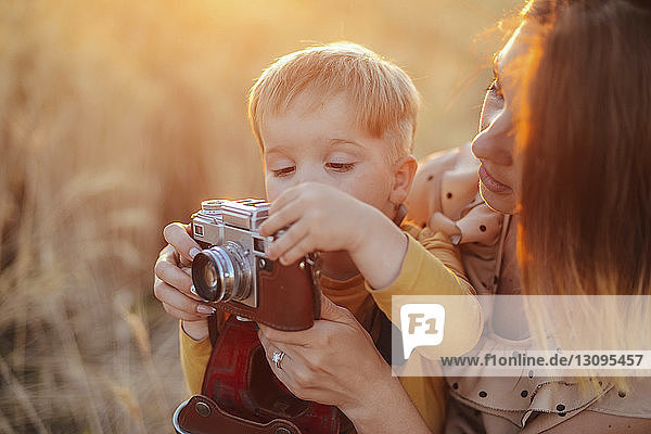 Son photographing with vintage camera by mother on field