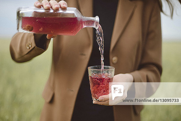 Mittelteil einer Frau  die stehend auf dem Spielfeld Getränke in ein Glas gießt