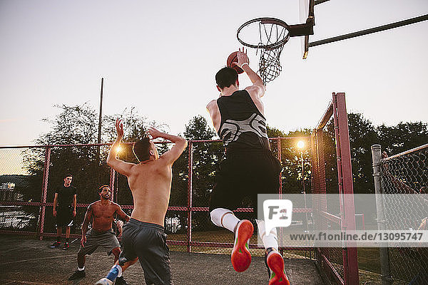 Männliche Freunde spielen bei Sonnenuntergang Basketball auf dem Platz
