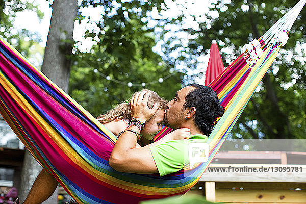 Mann küsst Tochter auf die Stirn  während er sich in Hängematte im Hinterhof entspannt