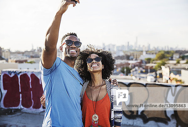 Couple in sunglasses taking selfie against sky on building terrace