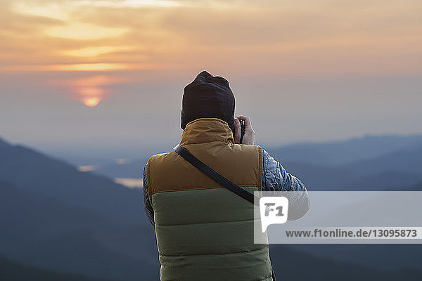 Rückansicht eines männlichen Wanderers  der bei Sonnenuntergang Berge fotografiert