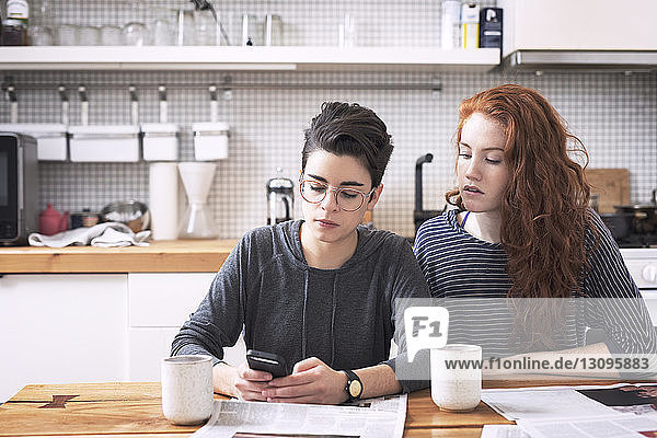 Lesbian using mobile phone while sitting with girlfriend at dining table