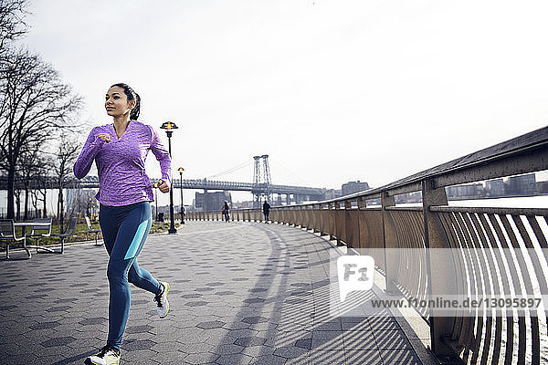 Entschlossene Athletin läuft auf einem Fußweg mit der Williamsburg Bridge im Hintergrund