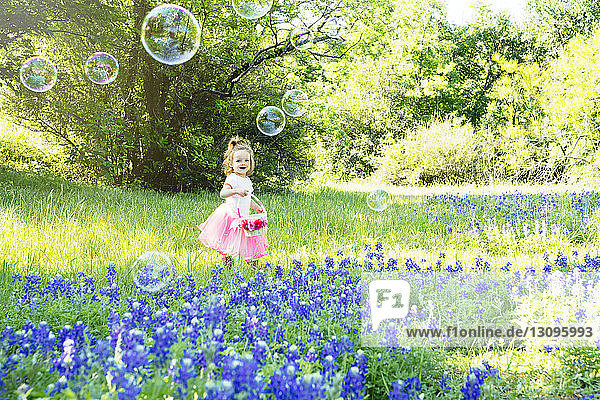 Lächelndes Mädchen schaut auf Blasen  während es bei den auf dem Feld blühenden Blumen steht