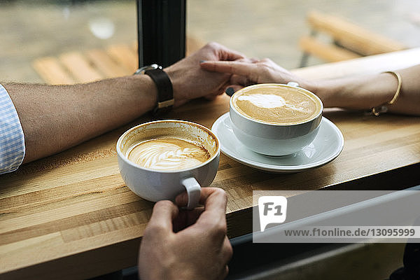 Beschnittenes Bild eines Paares  das sich bei einem Kaffee auf einem Tisch im Café an der Hand hält