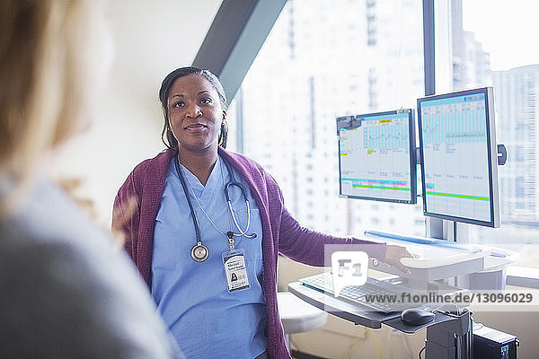 Ärztin  die den Patienten ansieht  während sie im Behandlungszimmer an den Desktop-Computern steht