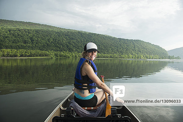 Portrait of smiling woman canoeing on river against cloudy sky