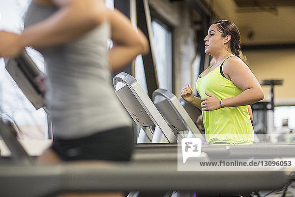 Midsection of woman with friend exercising on treadmills in gym