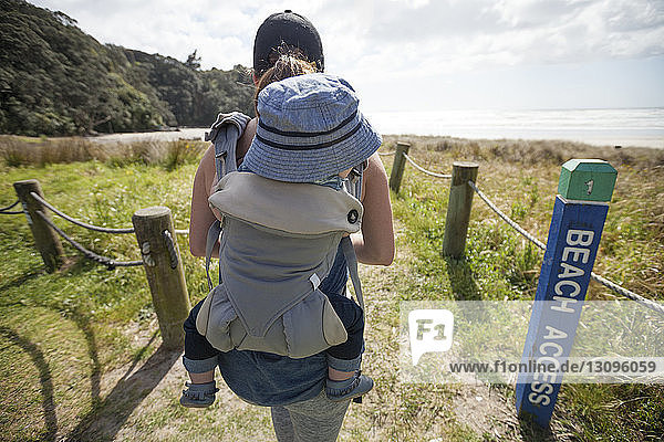 Rear view of mother carrying son in baby carrier while walking at beach