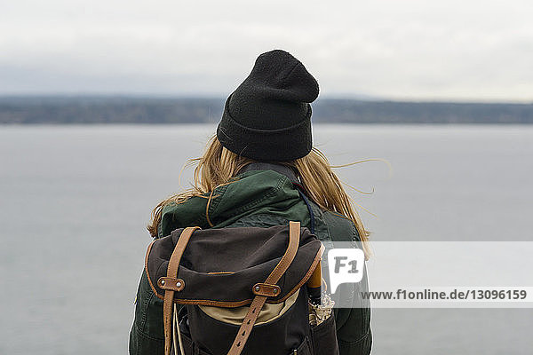 Rückansicht einer Frau mit Rucksack  die am Meer vor bewölktem Himmel im Discovery Park steht