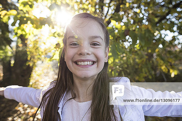 Close-up portrait of smiling girl with arms outstretched standing at park