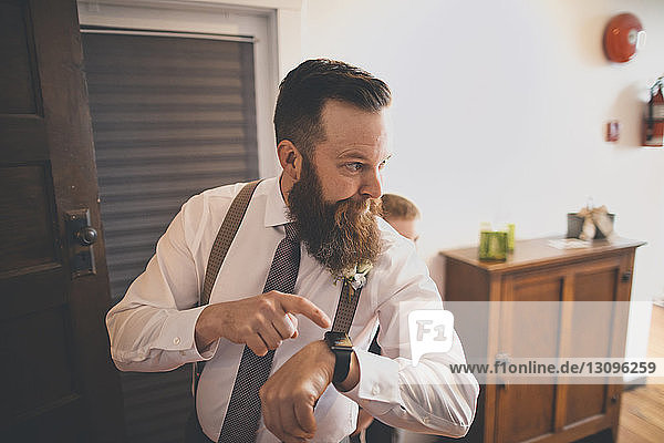 Bräutigam zeigt auf die Armbanduhr  während der Pagen zu Hause hinten steht