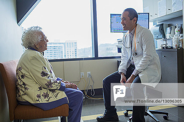 Lächelnder männlicher Arzt im Gespräch mit Patient auf der Krankenhausstation