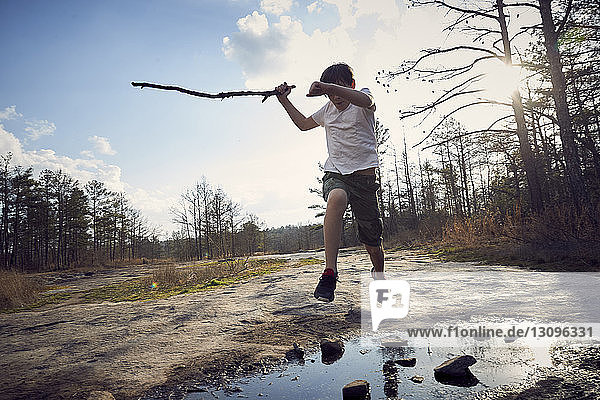 Boy jumping over puddle on Arabia Mountain against cloudy sky