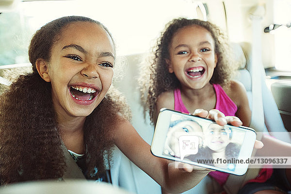 Glückliches Mädchen zeigt Foto in Smartphone  während es mit seiner Schwester unterwegs ist