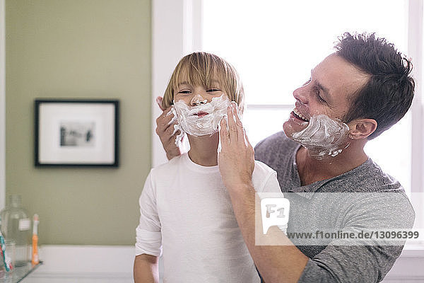 Father applying shaving cream to son in bathroom