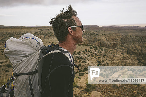 Seitenansicht eines Wanderers  der beim Tragen des Rucksacks vor einer halbtrockenen Landschaft wegschaut