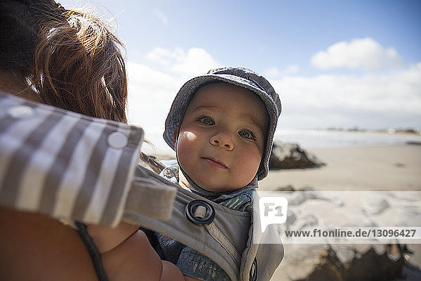 Ausgeschnittenes Bild einer Mutter  die einen Sohn in einer Babytrage am Strand trägt