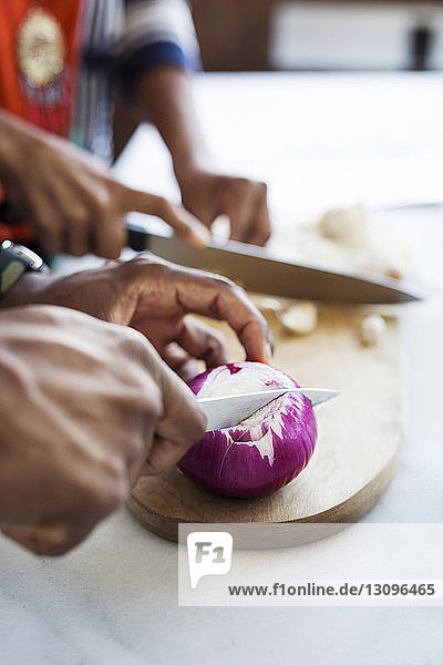 Ausgeschnittenes Bild eines Paares  das Zwiebel und Knoblauch in der Küche schneidet