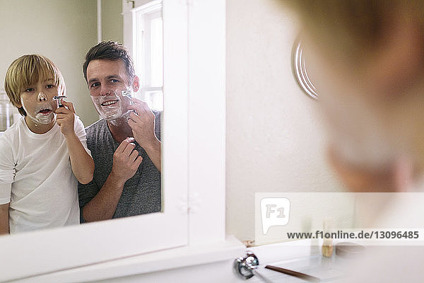 Vater und Sohn rasieren sich  während sie sich im Spiegel spiegeln