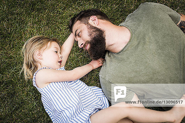 Hochwinkelaufnahme eines Vaters mit Tochter  die auf einem Grasfeld im Hof liegen