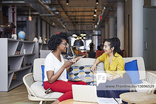 Businesswomen talking while sitting on sofa in creative office