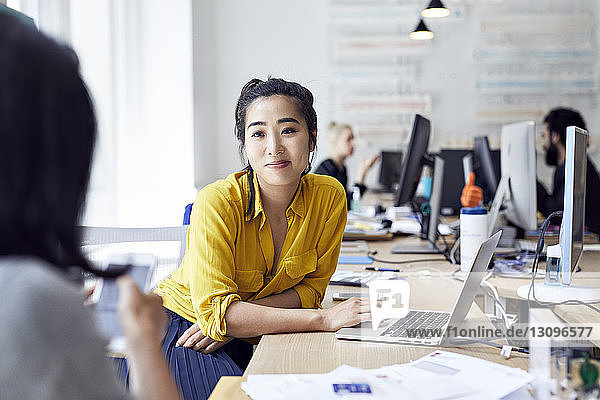 Businesswoman looking at female colleague with coworkers sitting in background