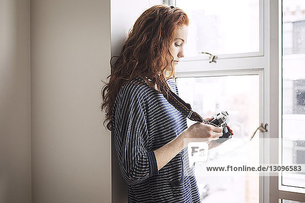 Frau benutzt Digitalkamera  während sie zu Hause am Fenster steht