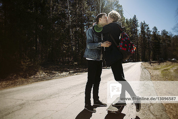 Romantic couple kissing while standing on road in forest during sunny day