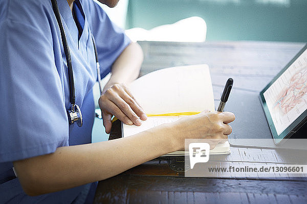Mittelteil einer Ärztin  die während ihrer Arbeit am Schreibtisch im Krankenhaus Tagebuch schreibt