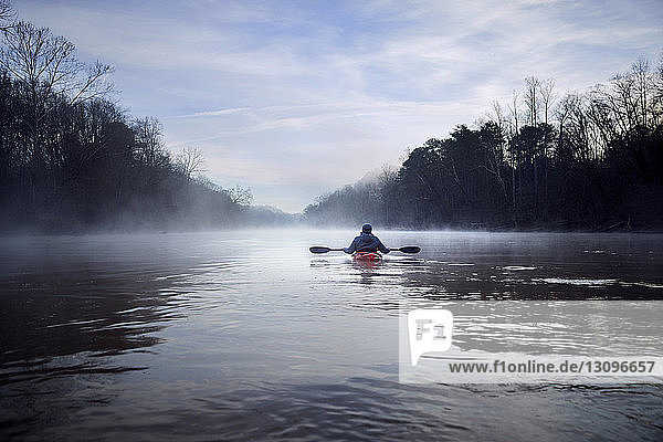 Rear view of man kayaking on Chattahoochee River amidst bare trees against sky