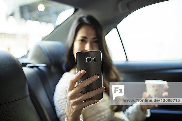 Young woman photographing through smart phone in taxi
