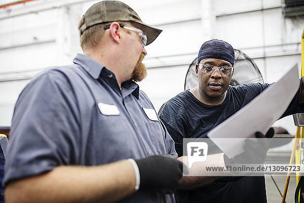 Arbeiter diskutieren über Dokument  während sie in einer Fabrik der Stahlindustrie stehen