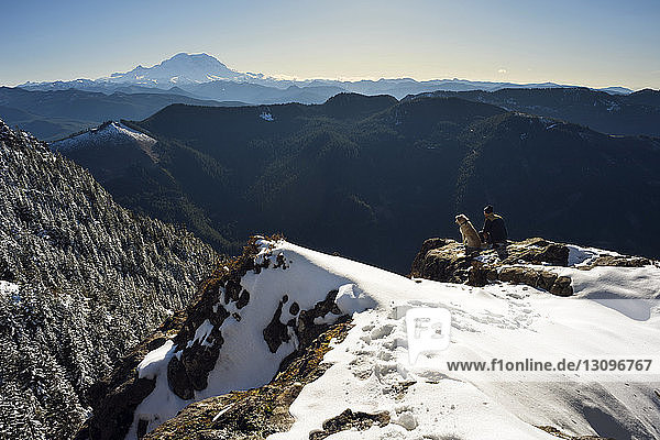High angle view of man sitting with dog on snowcapped mountain