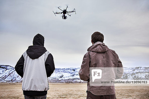 Rückansicht von Vater und Sohn  wie sie im Winter Drohne über das Feld fliegen