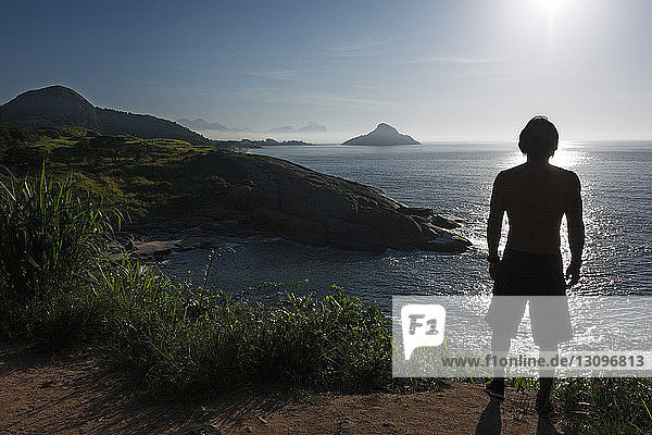 Rear view of silhouette man standing on cliff by sea against sky