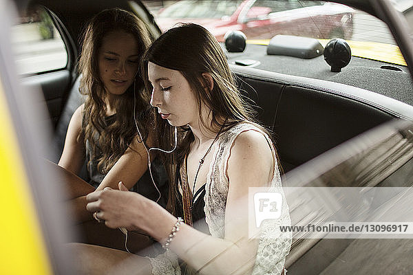Female friends listening music while traveling in taxi