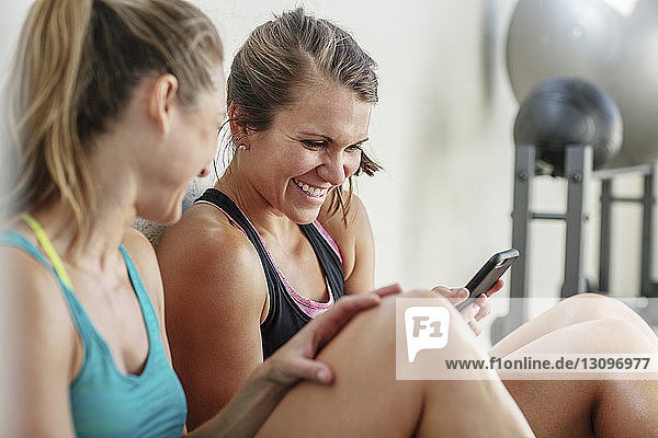 Happy female friends using mobile phone in gym