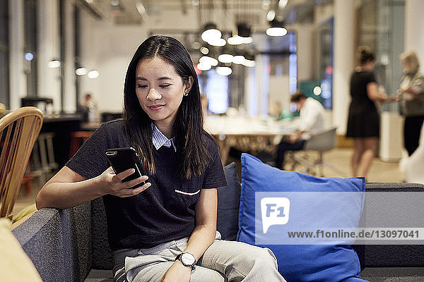 Selbstbewusste Geschäftsfrau benutzt Mobiltelefon  während sie im Kreativbüro auf dem Sofa sitzt