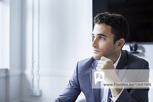 Thoughtful businessman looking away while sitting at board room in creative office